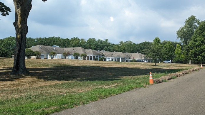 Exterior view of facility building and grounds photographed from distant tree-lined perimeter.