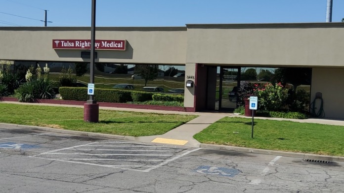 Exterior of treatment facility building with signage, landscaped grounds, parking area, and clear sky