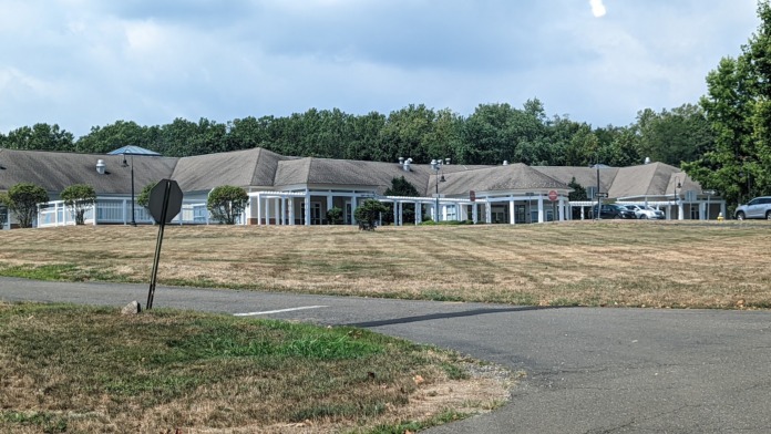 Exterior view of facility building with tan roof and multiple structures across open landscaped grounds.