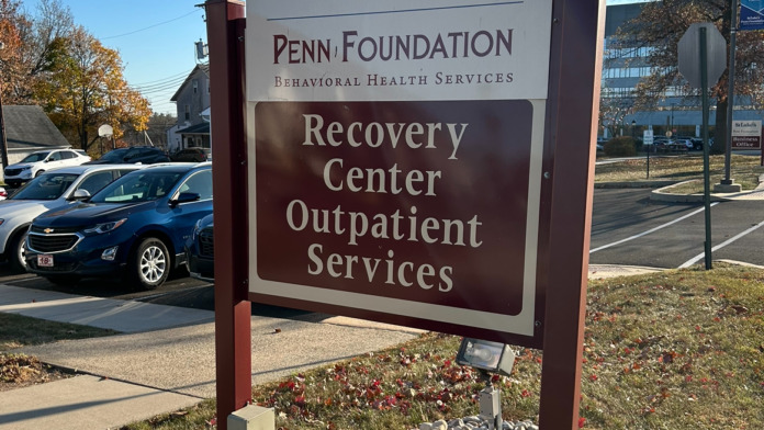 Exterior sign identifying Penn Foundation Behavioral Health Services Recovery Center with parking area and vehicles.