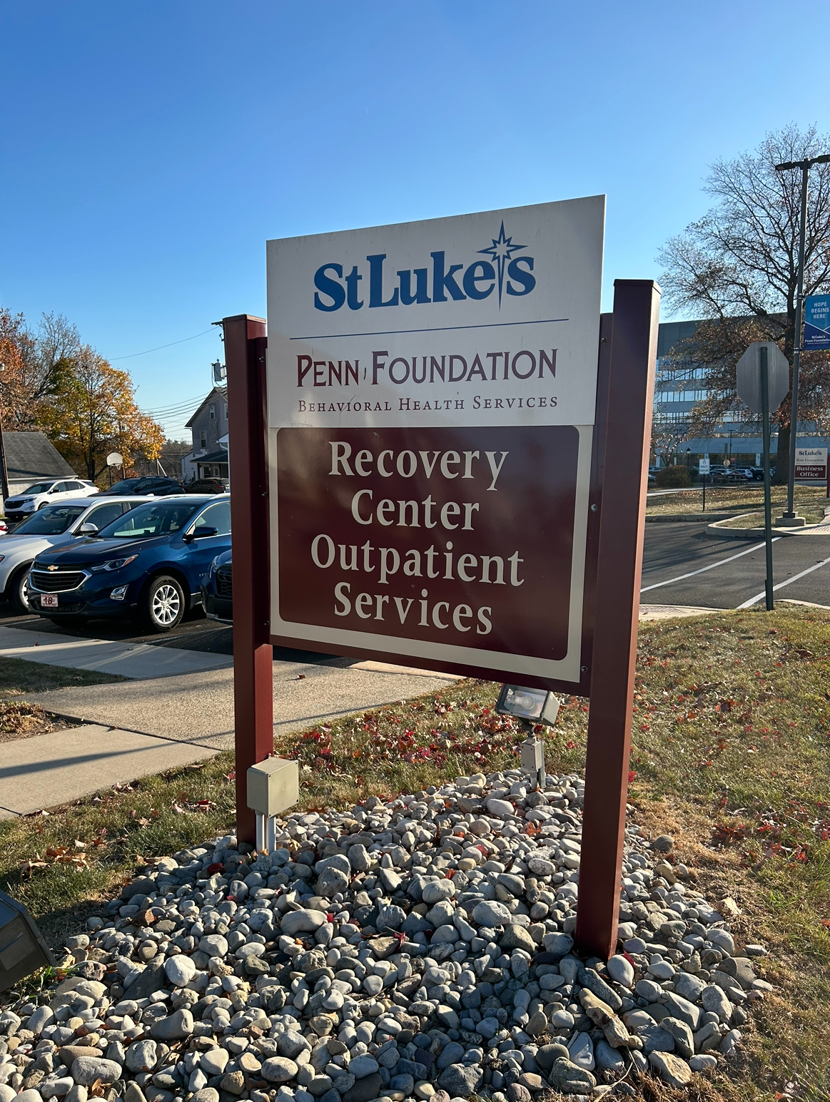 Exterior sign identifying Penn Foundation Behavioral Health Services Recovery Center with parking area and vehicles.