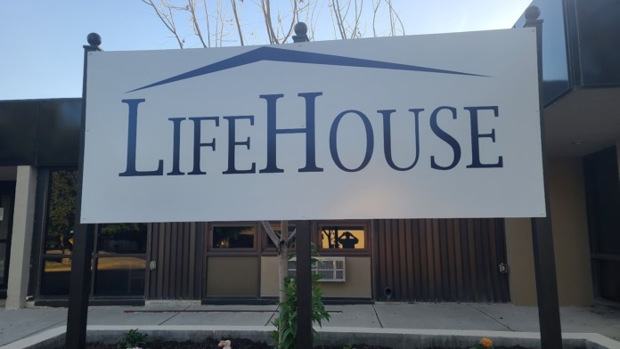 Exterior close-up of LifeHouse sign on white and blue mounted signage with building entrance and plantings below.