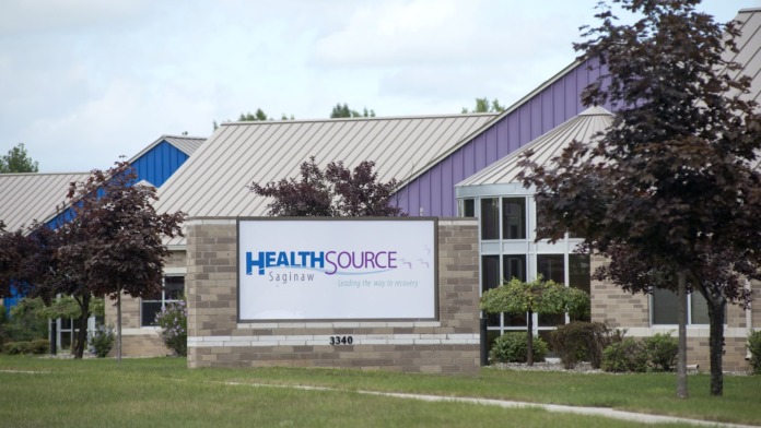 Exterior building facade with Health Source Saginaw signage, stone exterior, and landscaping