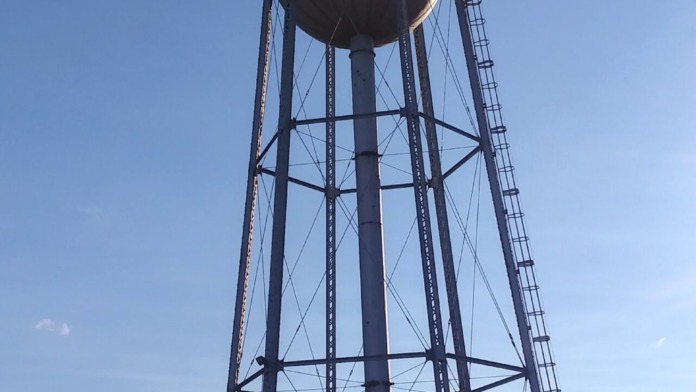Exterior water tower with metal framework and spherical tank against clear blue sky