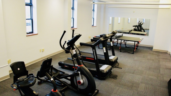 Interior fitness room with stationary exercise bikes, treadmills, table tennis, large mirror, windows with natural light, and carpeted flooring