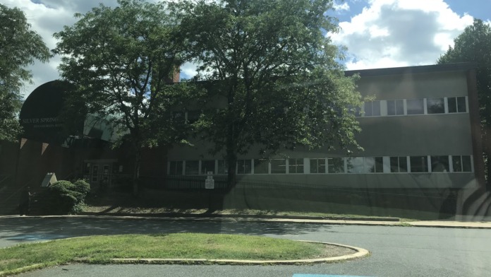 Exterior view of multi-story brick treatment facility building with windows, mature trees, and asphalt parking area.
