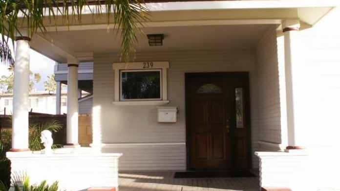 Exterior front entrance with columns, door numbered 239, and covered portico under palm tree overhang.