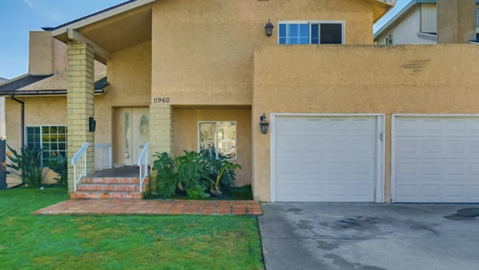 Exterior two-story residential home with yellow stucco, white garage doors, brick steps, and landscaping.