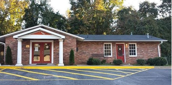 Exterior view of brick treatment facility with peaked white roof, columned entrance portico, and parking lot
