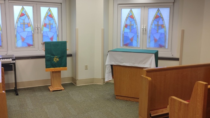 Interior chapel sanctuary showing pews, altar with religious furnishings, and multiple stained glass windows