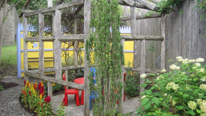 Outdoor garden space with wooden pergola structure, climbing vines, colorful seating, and flowering plants