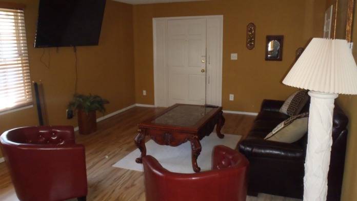 Interior common room with gold walls, red leather armchair, black sofa, wooden coffee table, and wall television