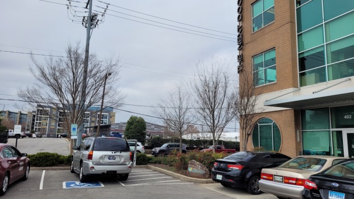 Exterior parking area showing facility entrance with turquoise windows, vehicles, and ground-level landscaping.