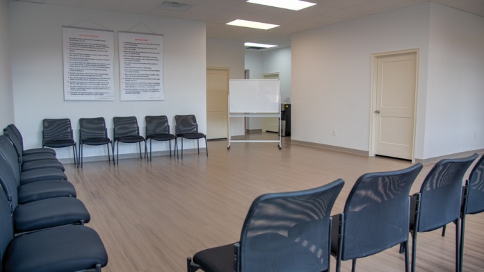 Meeting space with arranged black chairs, whiteboard, informational posters, and wood flooring