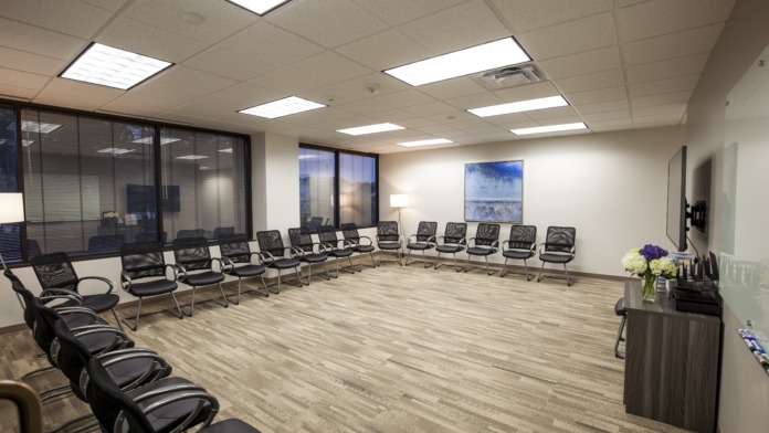 Interior large group therapy room with multiple black leather chairs arranged in semi-circle and mounted wall art