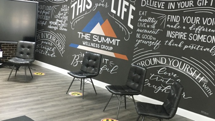 Interior therapy space with chairs, floor markers, facility logo, and inspirational wall messaging for group sessions