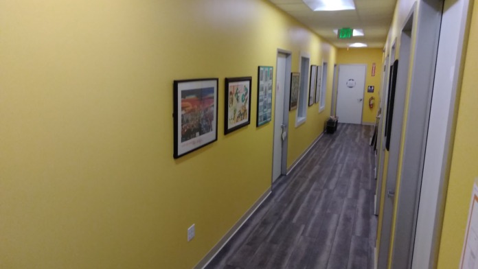 Interior hallway with yellow walls, framed artwork, dark flooring, and multiple doors along corridor.