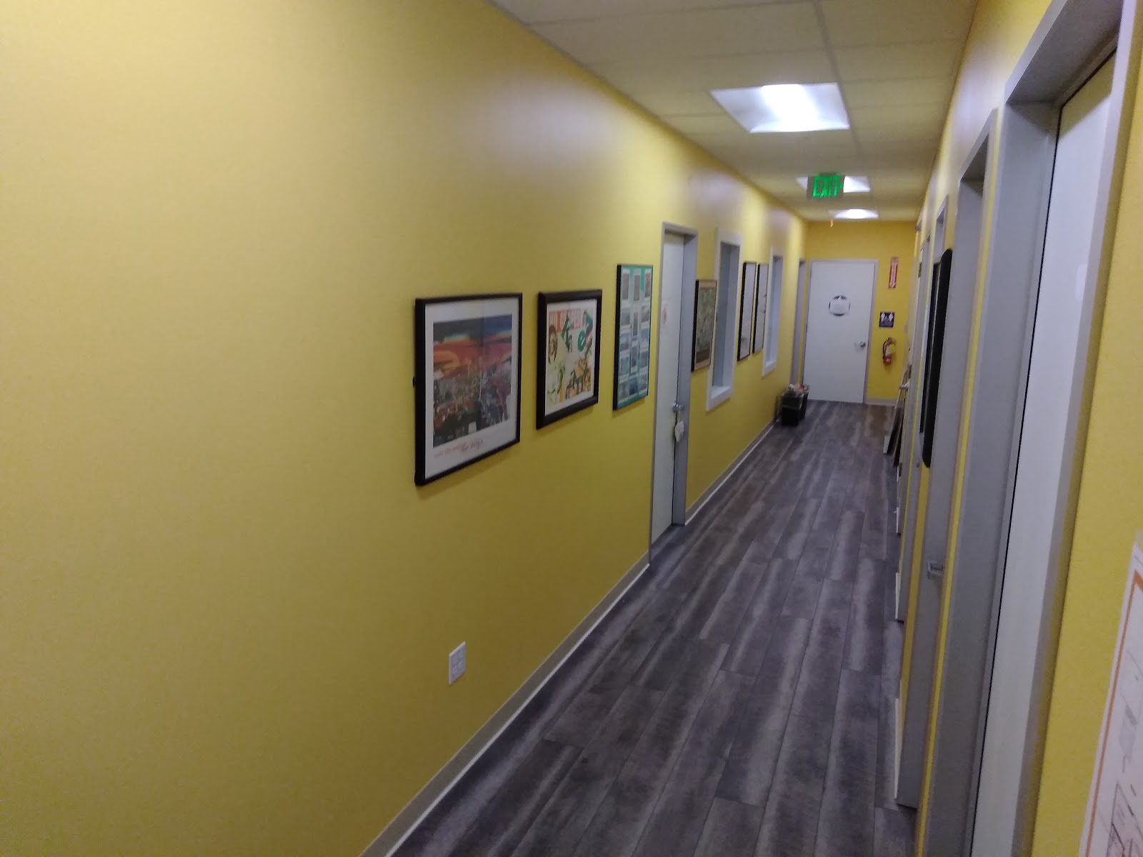 Interior hallway with yellow walls, framed artwork, dark flooring, and multiple doors along corridor.