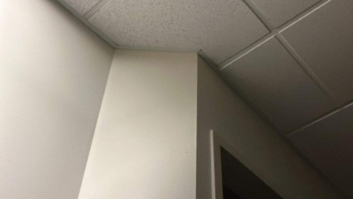 Interior corridor with suspended ceiling tiles, white walls, and mounted cross decoration