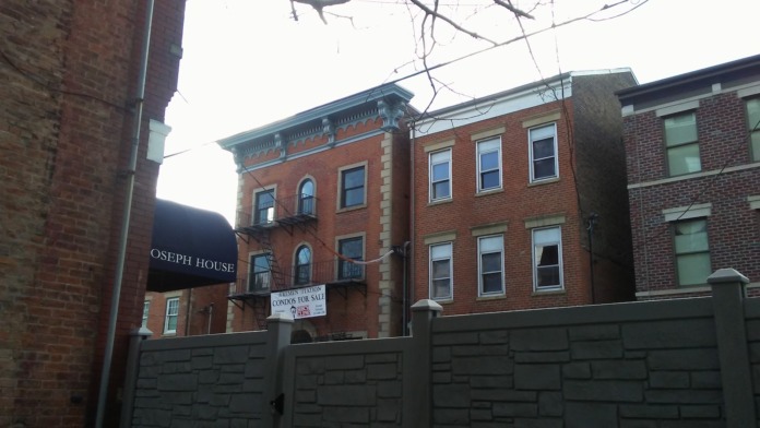 Exterior historic red brick Joseph House building with white architectural trim viewed behind protective fence