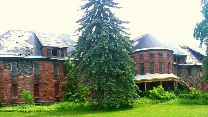 Exterior of brick institutional building featuring turrets, curved porches, and ivy coverage with landscaped grounds