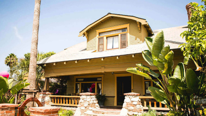 Exterior of yellow and green wood-siding house with decorative front porch and stone pillars