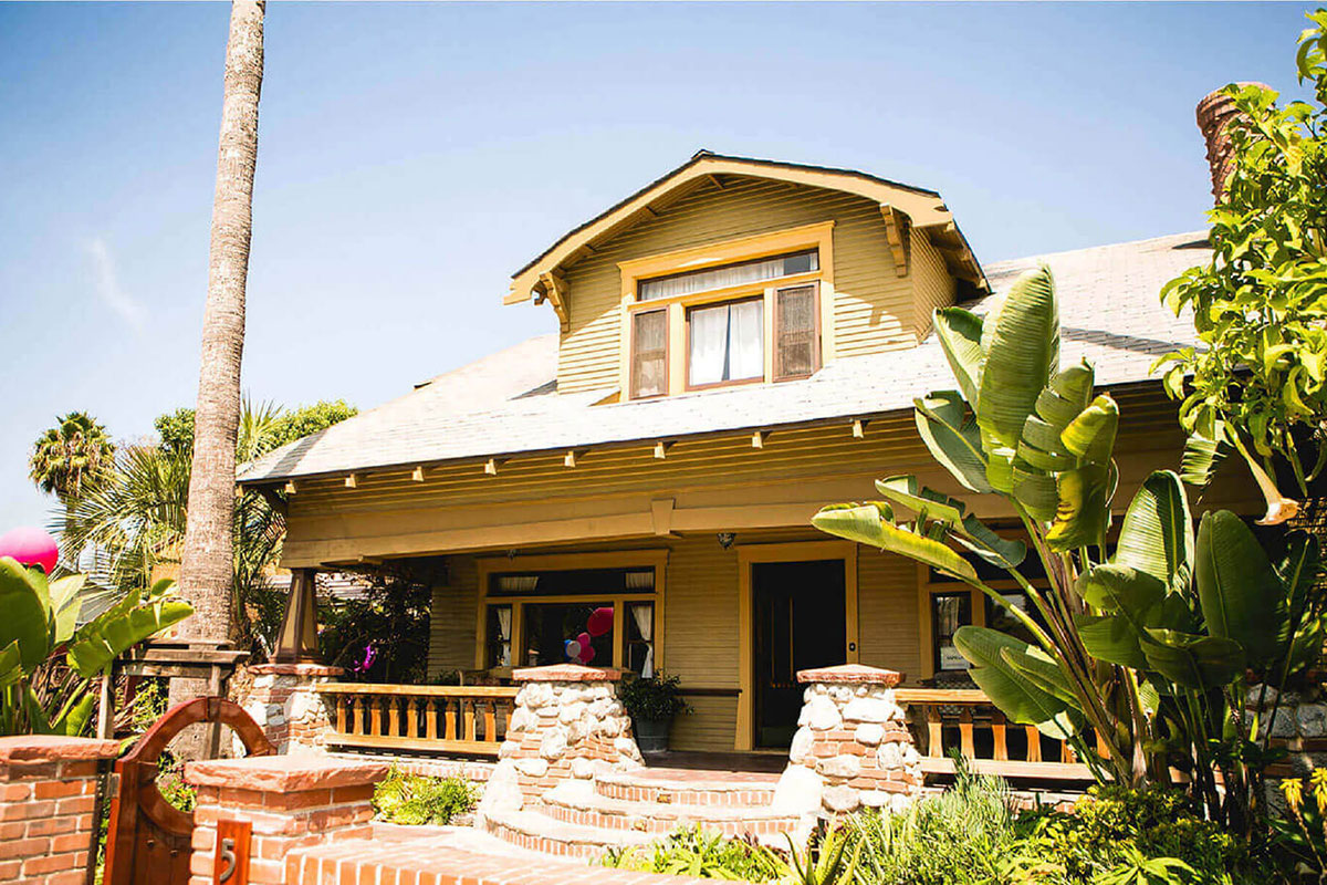 Exterior of yellow and green wood-siding house with decorative front porch and stone pillars
