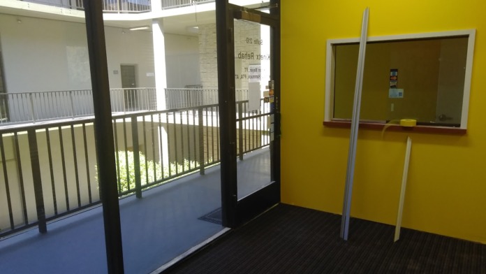 Interior room with yellow walls, glass door and panel openings, views to multi-story atrium with railings.
