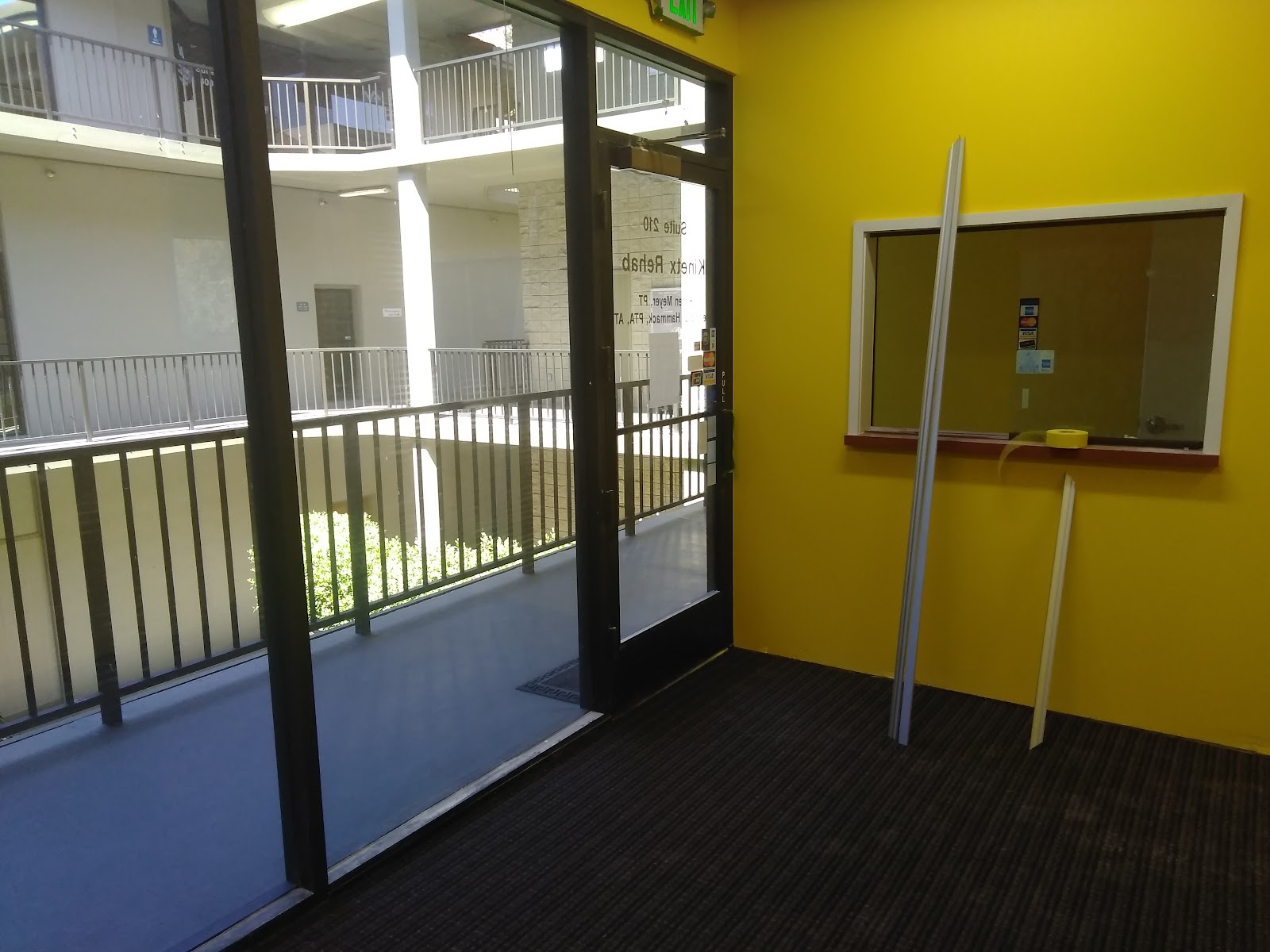 Interior room with yellow walls, glass door and panel openings, views to multi-story atrium with railings.
