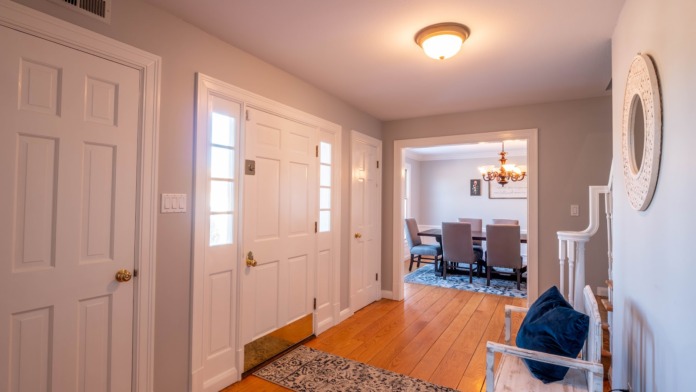 Interior hallway with light-colored walls, multiple closed doors, hardwood flooring, and opening to dining area.