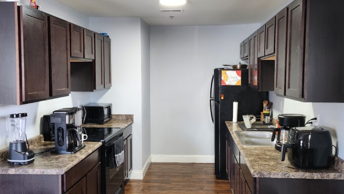 Interior galley kitchen with dark cabinets, granite countertops, stainless steel appliances, and hardwood floor