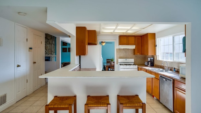 Interior kitchen featuring white island counter with wooden stools, cabinetry, and tile flooring.