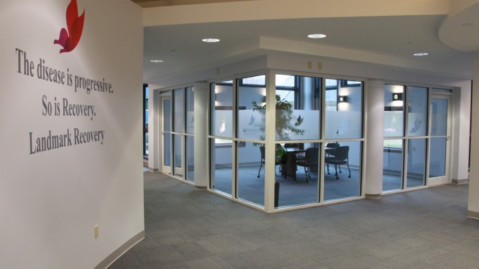 Interior entrance corridor with large glass doors and windows, wall signage reading recovery messaging, facility branding on glass, and tiled flooring