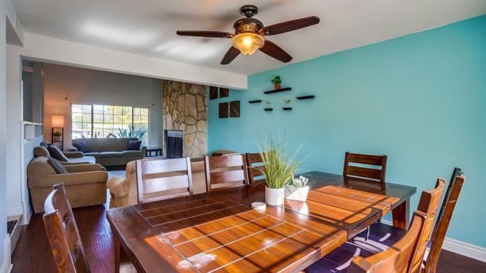 Interior view of living room with turquoise accent wall, wooden dining table, sofa, and stone fireplace.