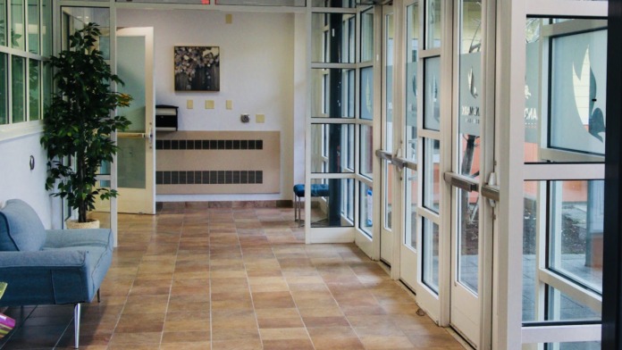 Interior lobby area with tiled flooring, glass entry doors, reception desk with filing system, chair seating, and natural lighting from windows