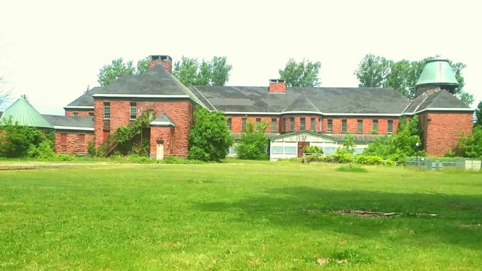 Exterior view of brick building with multiple chimneys, copper roof elements, and manicured lawn