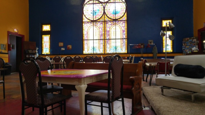 Interior community space with ornate stained glass windows, blue walls, wooden furniture, and high ceilings.