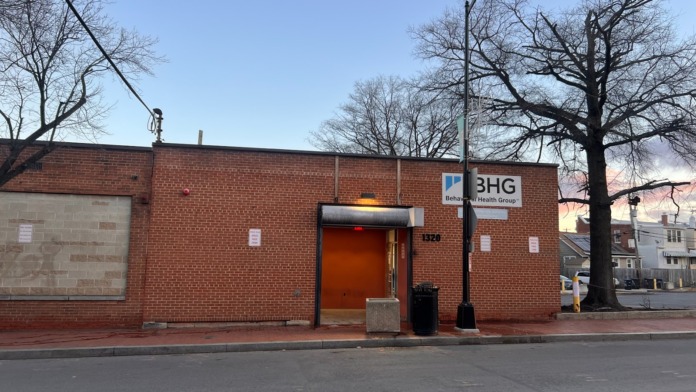 Exterior of brick treatment facility building showing main orange door entrance, BHG signage, and street view