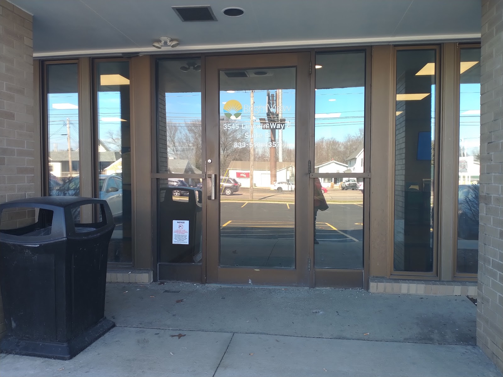 Exterior glass entry doors with tan brick walls and wood trim surrounding main entrance.
