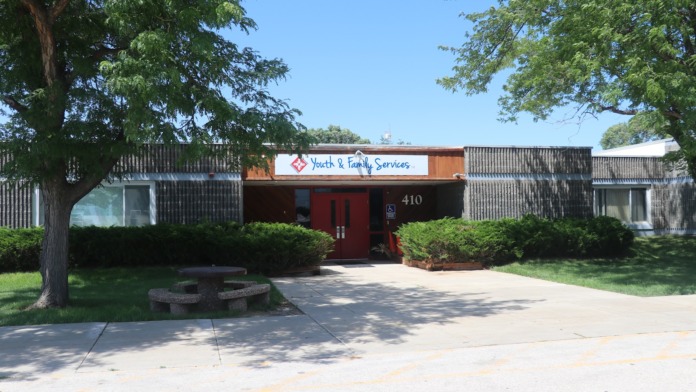 Exterior of Youth & Family Services building showing red entrance door, signage, address 410, landscaping, and trees.