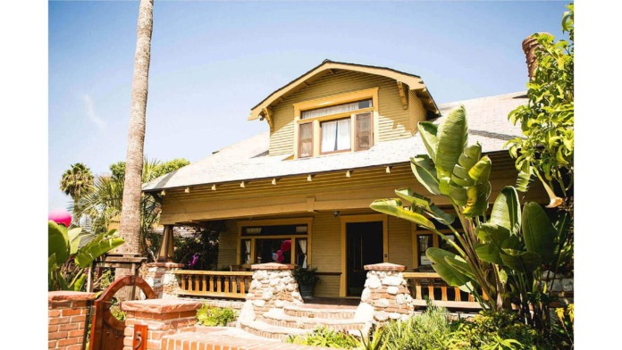 Exterior of two-story home with tan siding, wood trim, front porch with stone pillars, and tropical landscaping