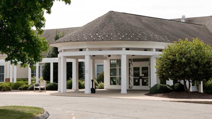 Exterior entrance portico with white columns, pitched roof, glass doors, and landscaped grounds.