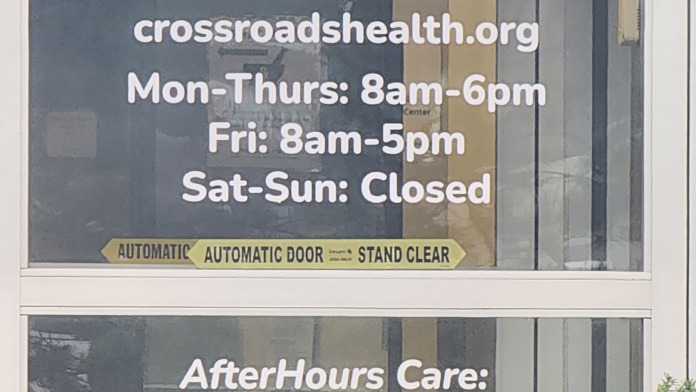 Exterior entrance door displaying Crossroads Health branding, phone number, website, and operational hours information.