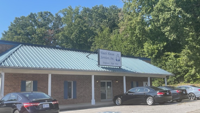 Exterior of treatment center showing main entrance with signage, brick and white siding, covered portico, and parking area