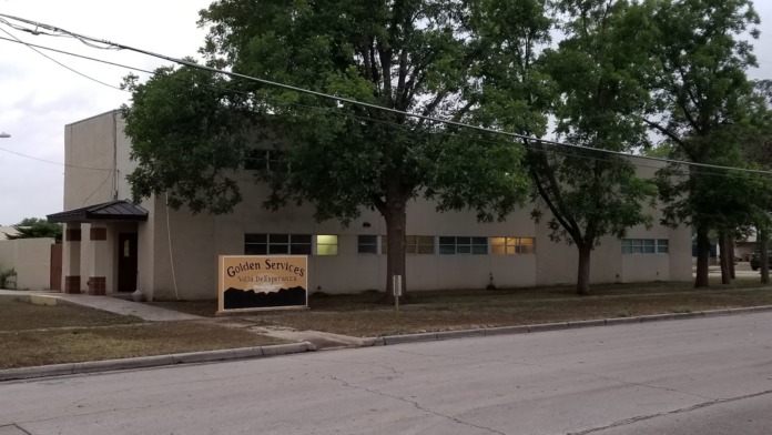 Exterior of treatment facility showing tan brick building with covered entrance, windows, trees, and street view.