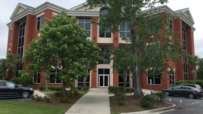 Exterior view of three-story red brick treatment facility building with landscaped grounds, multiple windows, and visitor parking area.