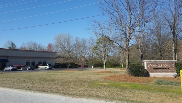 Exterior view of Cornerstone facility showing single-story building, parking area, landscaped grounds with trees and signage.
