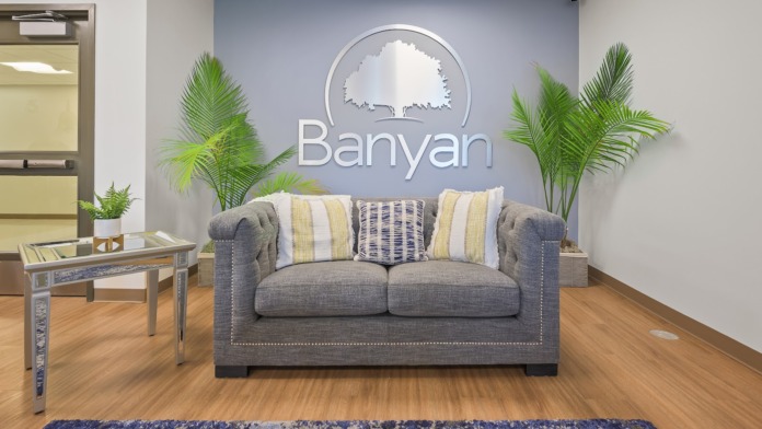 Interior reception area with gray sofa, decorative pillows, potted plants, and Banyan branding on accent wall