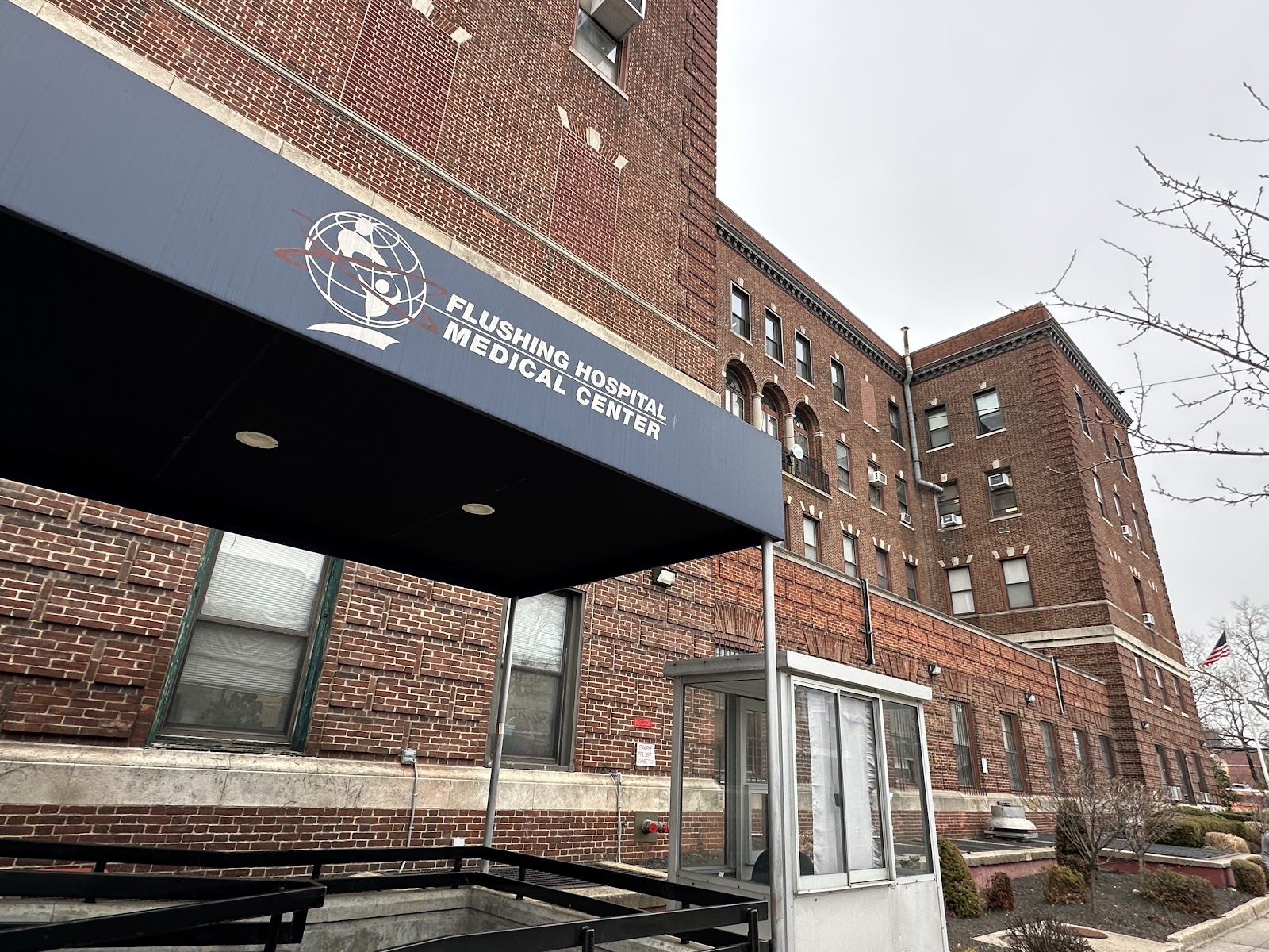 Exterior entrance with Flushing Hospital Medical Center blue awning, brick facade, and glass doors.