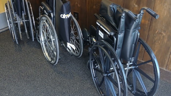 Interior hallway with wheelchairs and mobility aids stored against wood-paneled walls and yellow upper wall sections.